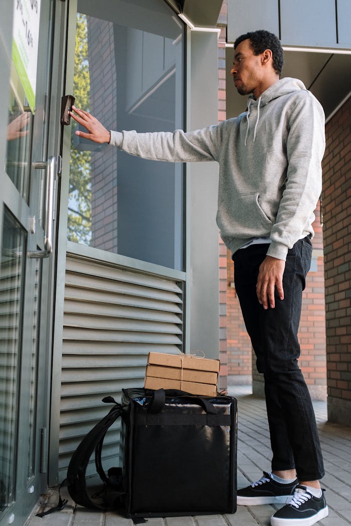 Services Male courier ringing doorbell for food delivery at modern building entrance.