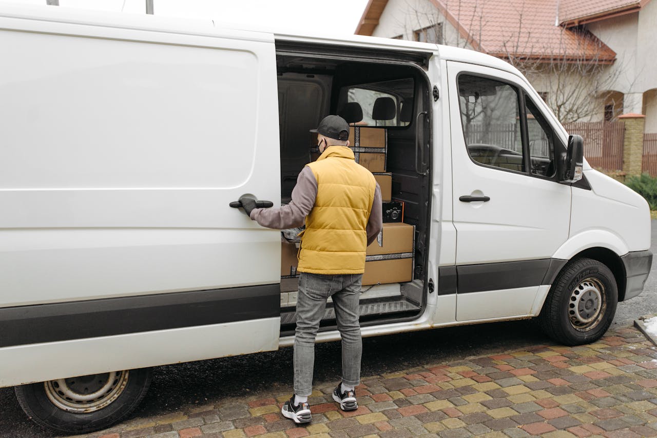 Services A delivery driver loads packages into a white van on a residential street.